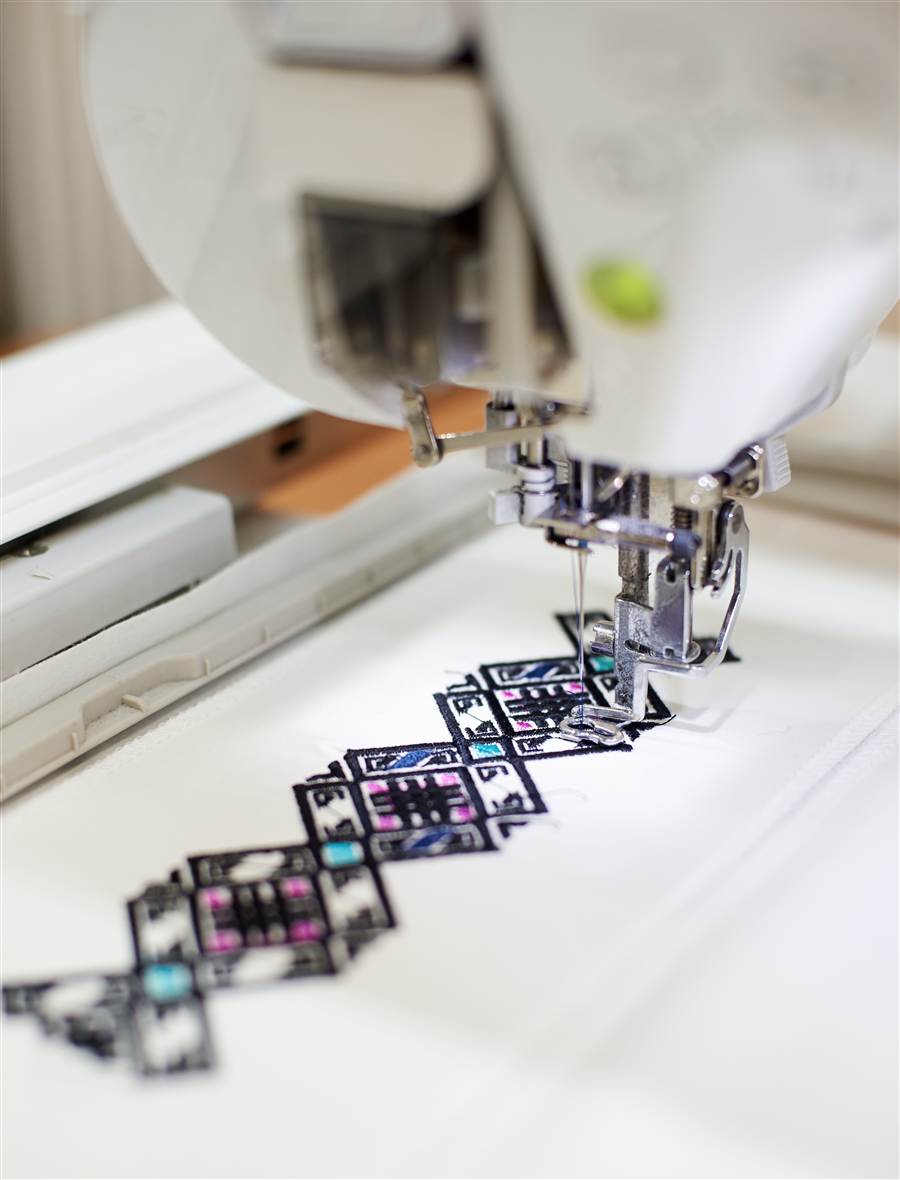 Hands guiding blue fabric under an embroidery machine needle