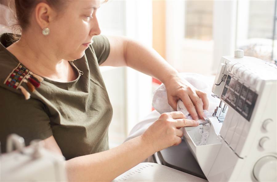 Person guiding pale fabric through a white serger